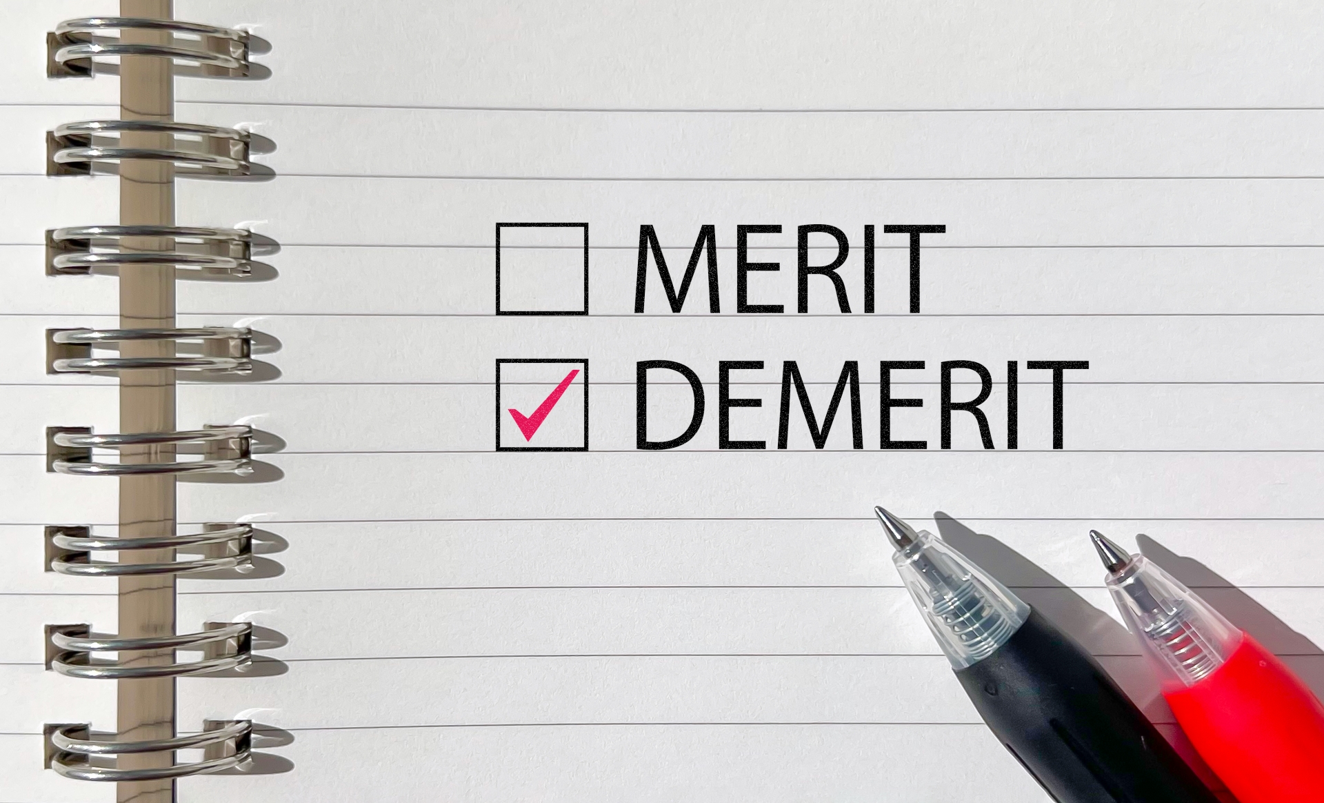 「DEMERIT」にチェックがつけられたノートとペン