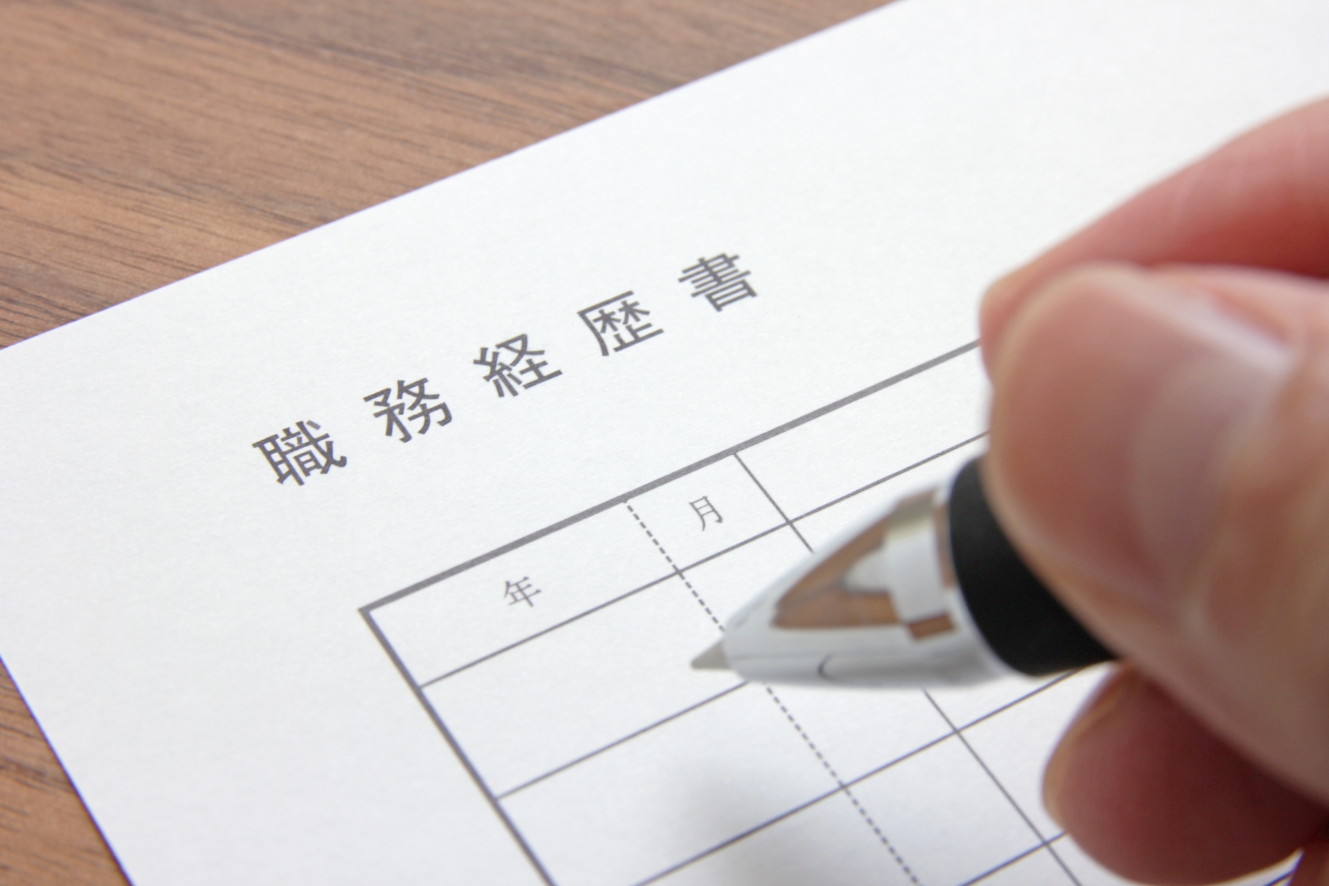 職務経歴書にペンで記入しようとする手